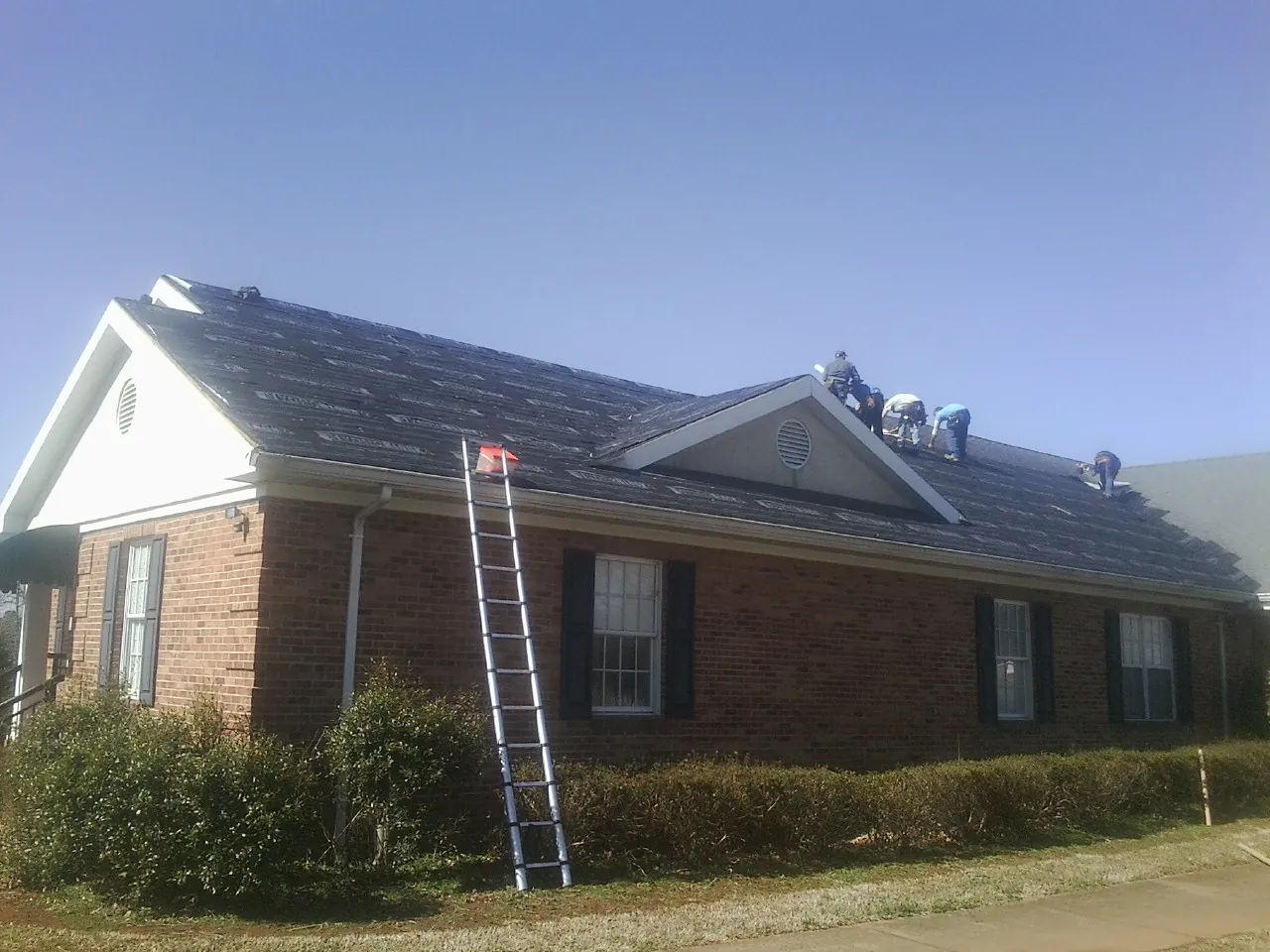 Crew tearing shingles off a brick ranch roof with a ladder set — Metal Roof Repair work by our crew in Munroe Falls