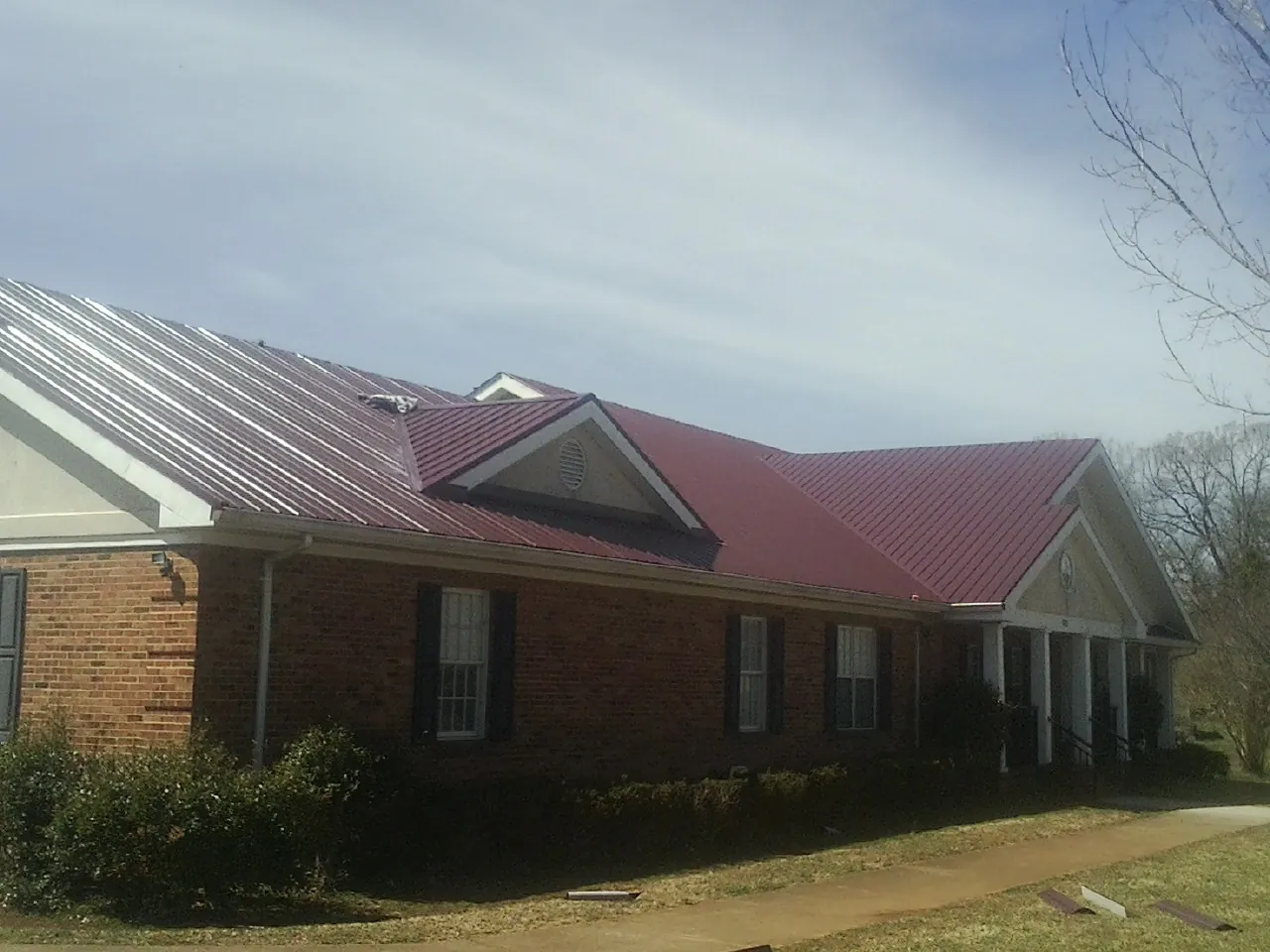 Red metal roof with gabled entries on a long brick building, from a Hail Damage Roof Repair job in Munroe Falls