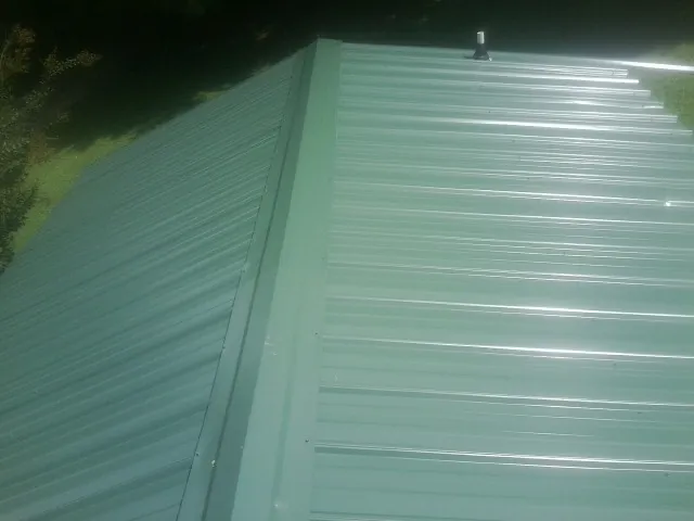 New green metal panels meeting at the ridge of a roof — Flat Roof Repair work by our crew in Munroe Falls