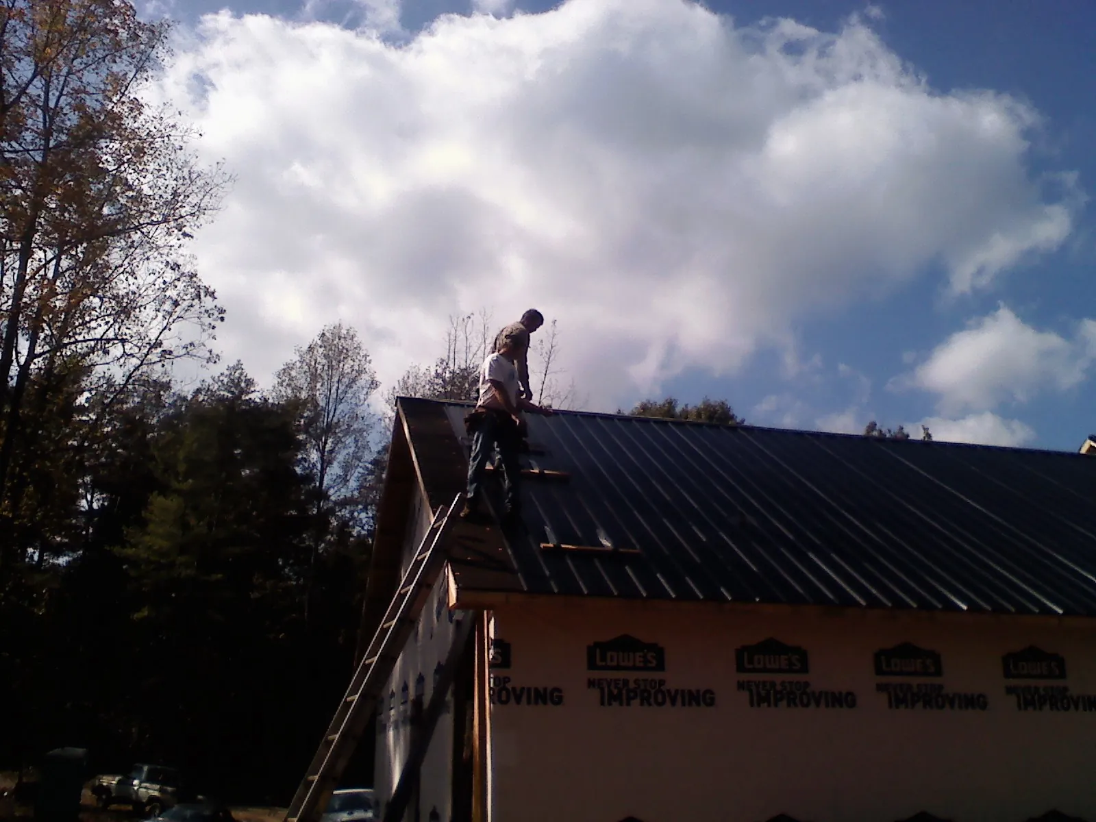 Roofer fastening dark metal panels high against a cloudy sky, from a Roof Inspection job in Munroe Falls