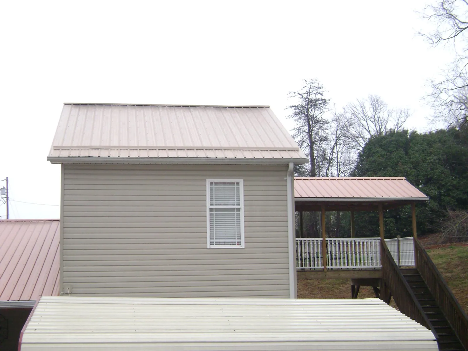 Tan metal roofs on a two story addition and attached porch, from a Roof Replacement job in Munroe Falls